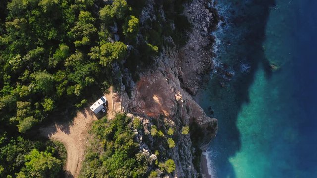 Top down view of a camper van parked on the edge of a rock with a beautiful view of the seaside and nature. Couple chilling and relaxing.