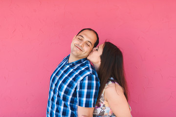 woman kissing man at pink wall