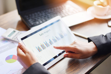 Business woman working in office with checking business report using tablet computer technology laptop with calculator and coffee cup - Sale report money analyzing graphs chart