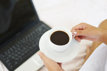 Morning coffee cup top view - woman holding coffee cup by hand with laptop on the bed