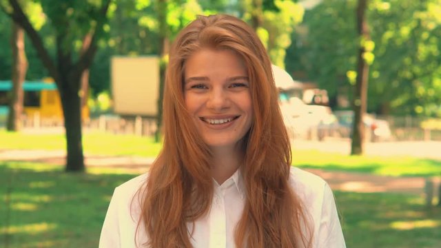 portrait caucasian girl standing on the street looking at the camera and laughing teeager wearing white casual shirt posing outdoors