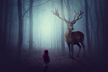 Kleines KInd steht vor einem großen Hirsch im dunklen mystischen Wald