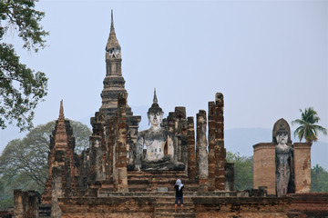 Fototapeta premium male tourist in east headscarf is looking on big budda statue famous Sukhothai Historical Park, a UNESCO World Heritage Site, Foggy spring day in the ancient capital of Sukhothai. Thailand