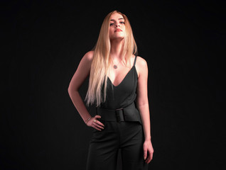 Blonde woman in black overall standing over black background