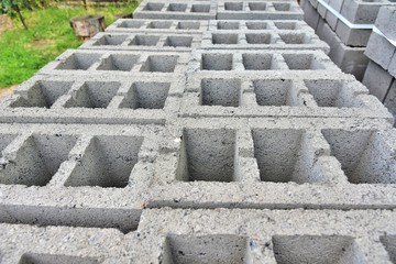 Stack of gray textured cinder blocks for house or fence building. Construction Materials. Pallet with cinderblocks and pile of sand on background. Row of grey concrete bricks. Brickwork 