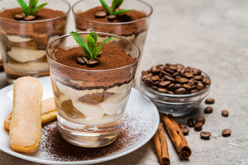 Classic tiramisu dessert in a glass cup and savoiardi cookies on plate on concrete background