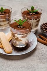 Classic tiramisu dessert in a glass cup and savoiardi cookies on plate on concrete background