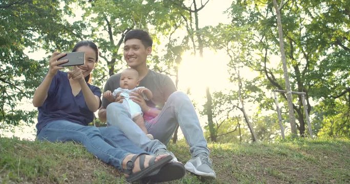Father and Mother using smartphone to selfie with baby son at park. Asian family having quality time together. People with Family concept.