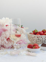 A glass of sparking wine with strawberries for a birthday breakfast and peonies in the background