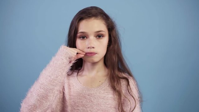 Caucasian teen girl against a blue background keeping a secret or asking for silence, zipping her mouth serious face, obedience concept