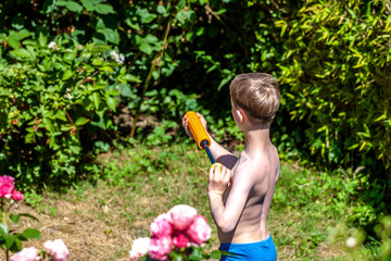 Happy little boy having fun with squirt gun in the garden