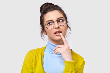 Closeup studio portrait of thoughtful young woman with a bun hairstyle, wearing casual outfit and...