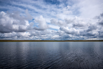 Naklejka na ściany i meble panoramic view of blue sky with white fluffy clouds reflecting on mirror water surface of amazing lake surrounded by hills 