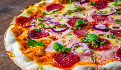 Obraz na płótnie Canvas Pizza with Mozzarella cheese, ham, tomato sauce, salami, onion, pepper, Spices and Fresh basil. Italian pizza on wooden table background