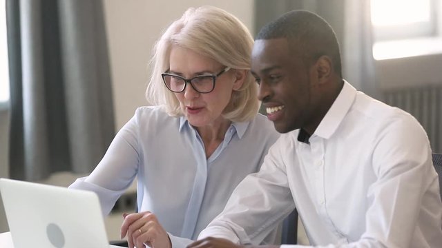 Old female manager teach young african intern explain computer work