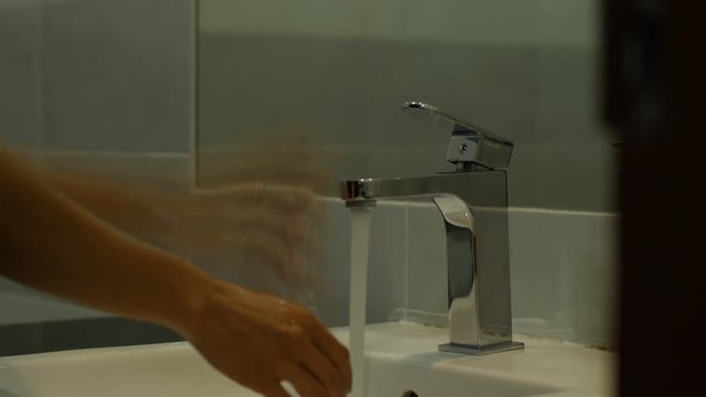 Woman washing her hands by water from faucet.