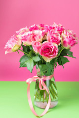 Bouquet of pink roses in a glass vase on a green and pink background. On a vase the red tape is tied.