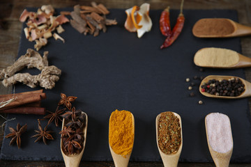 Traditional spices in wooden spoons on a black cutting board on a wooden rustic background with copy space for text and image. Healthy food. Vegan lifestyle. Flat lay, top view. Spices pattern.