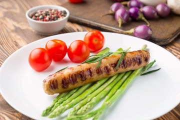 Fried sausage with asparagus on a white plate, wooden table.