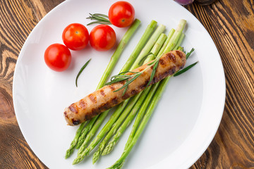 Fried sausage with asparagus on a white plate, wooden table.