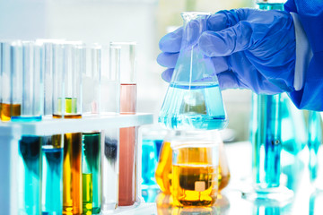 The scientist's hand holds a beaker of chemicals in the lab to prepare specimens to test in the laboratory blue background, science research and development concept