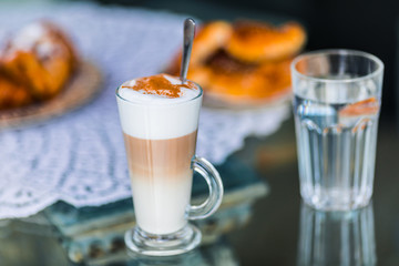Coffee latte in glass with milk foam and cocoa, cinnamon powder and cake bisquit for breakfast