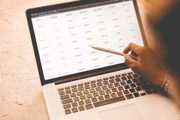 close up businessman hand with pan looking through the details of stock market on laptop