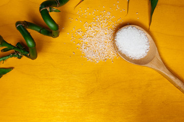 Coarse salt crystals and bamboo on a yellow table. Wooden spoon with sea salt. Background for advertising salty.