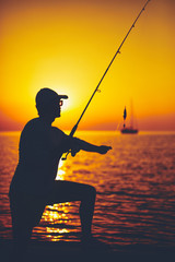 Silhouette of a fisherman fishing in sunset time on the open sea.