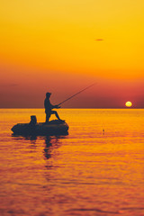 Silhouette of a fisherman fishing in sunset time on the open sea.