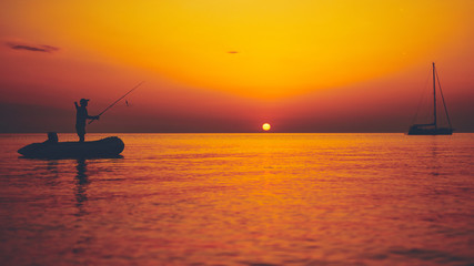 Silhouette of a fisherman fishing in sunset time on the open sea.