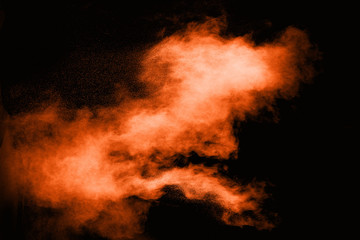 Freeze motion of orange powder exploding  on black background. Abstract design of color dust cloud. Particles explosion.