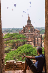 A young man sitting and looking at balloons in a temple at the lovely sunrise of Bagan, Myanmar. © unai