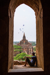 A young man sitting and looking at balloons in a temple at the lovely sunrise of Bagan, Myanmar. Vertical photo © unai