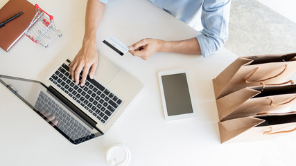 Man holding credit card in hand and entering security code using smart phone on laptop keyboard, online payment shopping concept