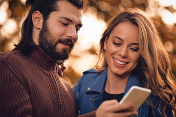 Young couple using cellphone in autumn colored park.