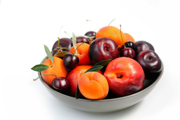 Naklejka na ściany i meble Fruit bowl. Seasonal fruits with green leaves in a bowl over white background, top view. Organic fresh fruit, peach, plum, aprocot, cherry.