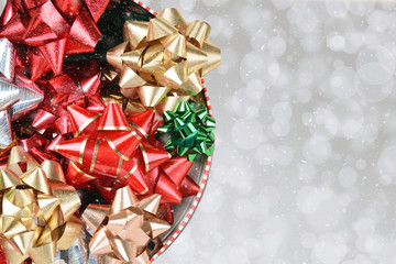 A tin of colorful Christmas bows on a silver bokeh background with snow effect and copy space. Shot from directly above.