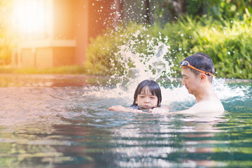 Daughter hold father's arm to practice swimming. Daddy teach kid girl to swim in natural resort hotel. Instructor give lesson child kick her legs to splash water in swimming pool.