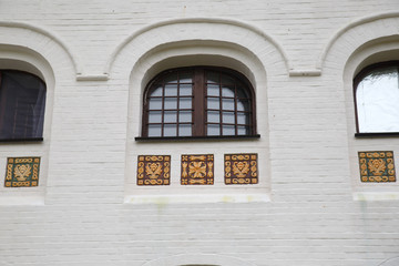Fragment of a white wall with windows and tiled decor.
