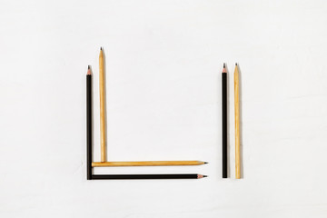 Geometric pencils folded on a white table. Black and yellow wooden pencils for drawing. Creative flat lay of workspace desk.  Copy space.