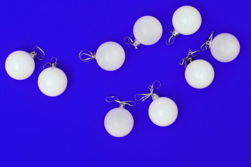 White Christmas balls ornaments on bright blue background. Flat lay New Year minimal decoration. Christmas card. Top view.