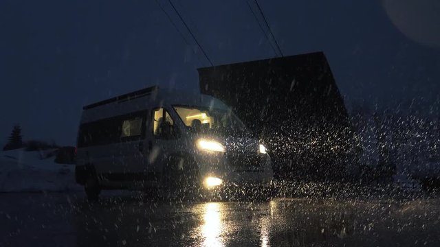 The white sleeping van parked in the middle of a snowstorm in winter. Big snowflakes are falling, lousy weather.