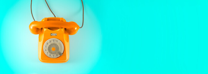 A orange vintage dial telephone with blue background.