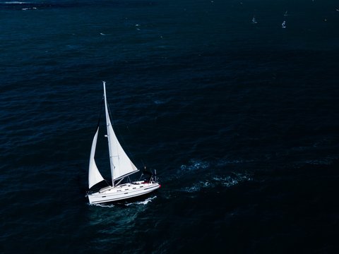 Aerial shot of a small white boat sailing in the ocean