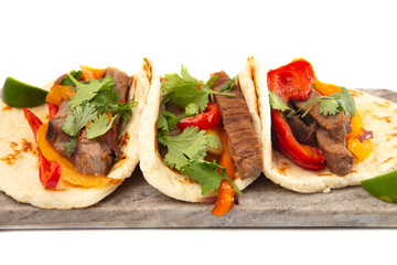 Three Fajitas on a Marble Serving Board on a White Background