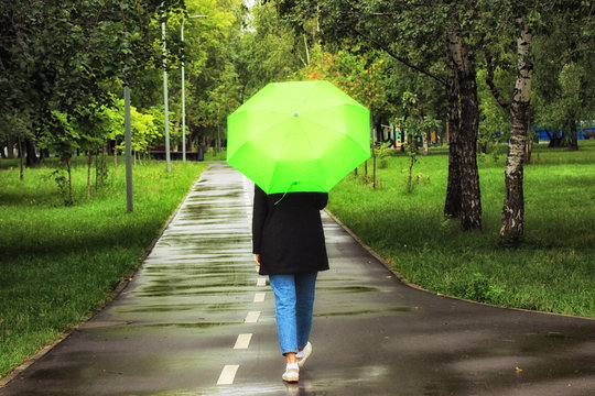 Young beautiful girl walking alone under green umbrella in the city park in summertime