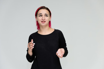 Portrait to the waist of a pretty girl with red hair on a white background in a black jacket. Standing right in front of the camera in a studio with emotions, talking, showing hands, smiling