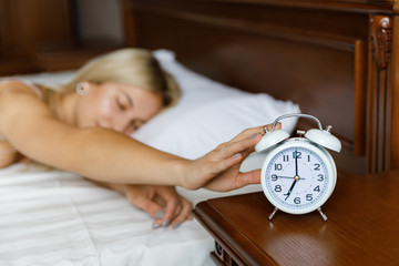 A young beautiful blonde girl wakes up in the morning, and wakes her alarm clock. The girl wakes up...