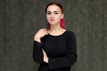 Portrait to the waist of a pretty girl with red hair on a gray background in a black jacket. Standing right in front of the camera in a studio with emotions, talking, showing hands, smiling